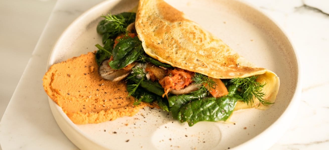 A folded omelette stuffed with some green leaves and tomato, resting on a white plate